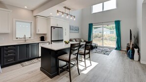 A modern kitchen with a central island, dark cabinetry, and a large window providing natural light. - Cozy, spacious family home w/ Arcade! 5 mins from Beach! (Port Stanley)