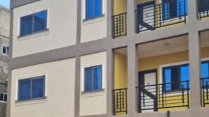 Un immeuble à plusieurs étages doté de balcons, de fenêtres et d’une zone au rez-de-chaussée dallée.