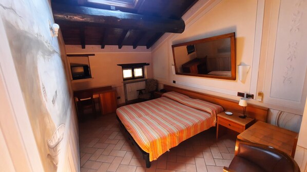 A compact bedroom with a single bed, a bedside table, a chair, a desk with a chair, a mirror, and a radiator. - Albergo Giulia Gonzaga (Sabbioneta)
