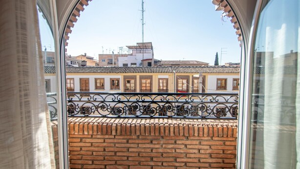A balcony with a brick wall and wrought iron railing, overlooking a row of buildings with traditional architecture. - Armilla Apartament by A3Rentals (Armilla)