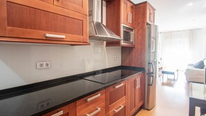 A modern kitchen with wooden cabinets, a black countertop, stainless steel appliances, and a view of a living area with a sofa and curtains. - Armilla Apartament by A3Rentals (Armilla)