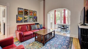 A living room with a red leather sofa, a wooden coffee table, and a patterned rug. There are framed pictures on the wall and a window with curtains. - Boise-Historical-Northend-Downtown-Franklin 101 (Boise)