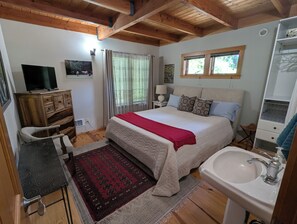A bedroom with a bed, a desk, a TV, a window, and a bathroom.