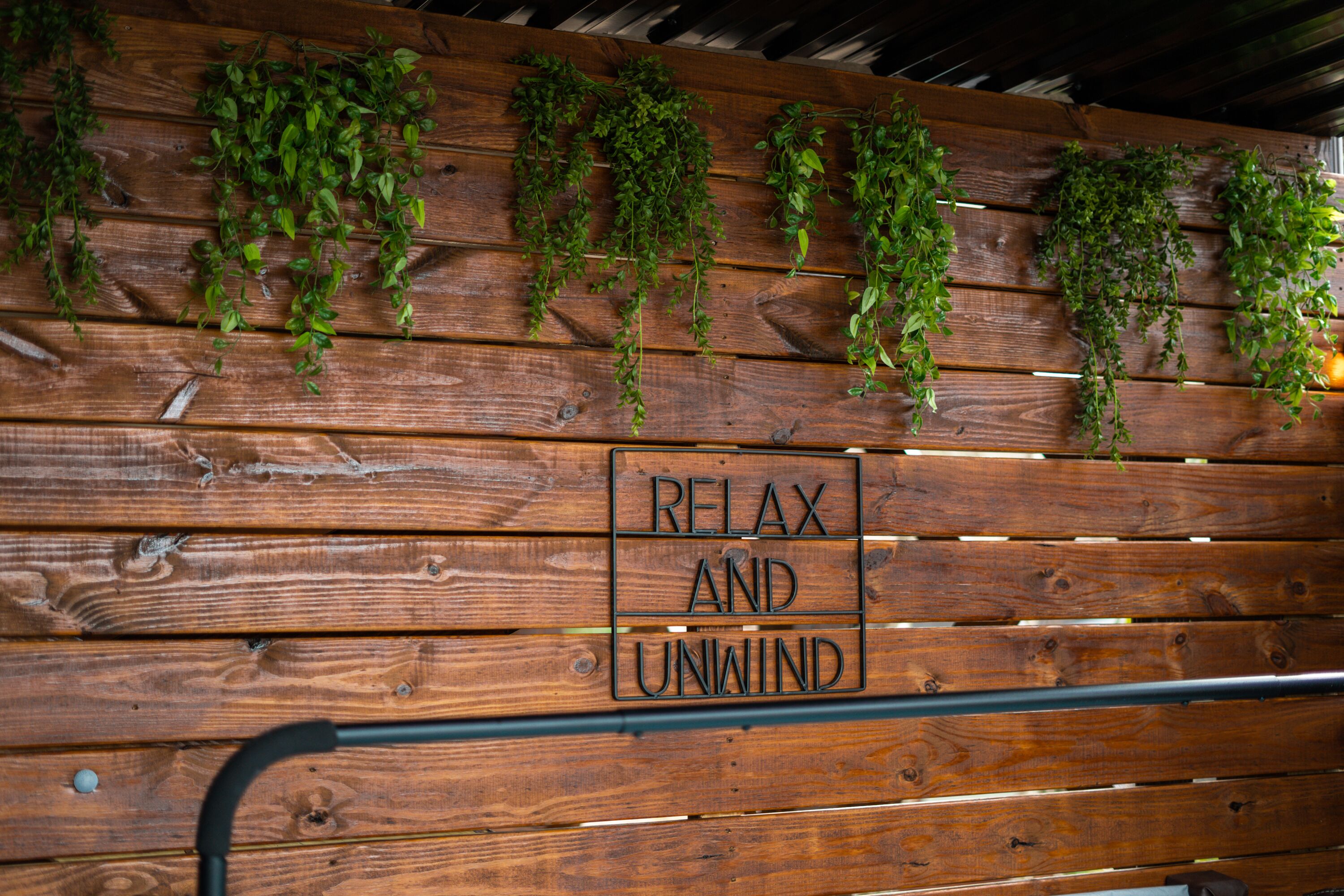 Un mur en bois orné de plantes vertes suspendues et d’une pancarte sur laquelle on peut lire : « DÉTENDEZ-VOUS ET RELÂCHEZ-VOUS ».