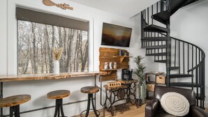 Una cocina moderna con barra de madera, escalera de caracol y un amplio ventanal con vistas a árboles.