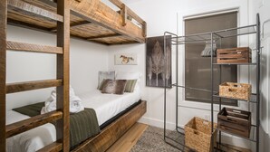 Una cama litera con estructura de madera, una estantería metálica con cestas y una ventana con vistas.