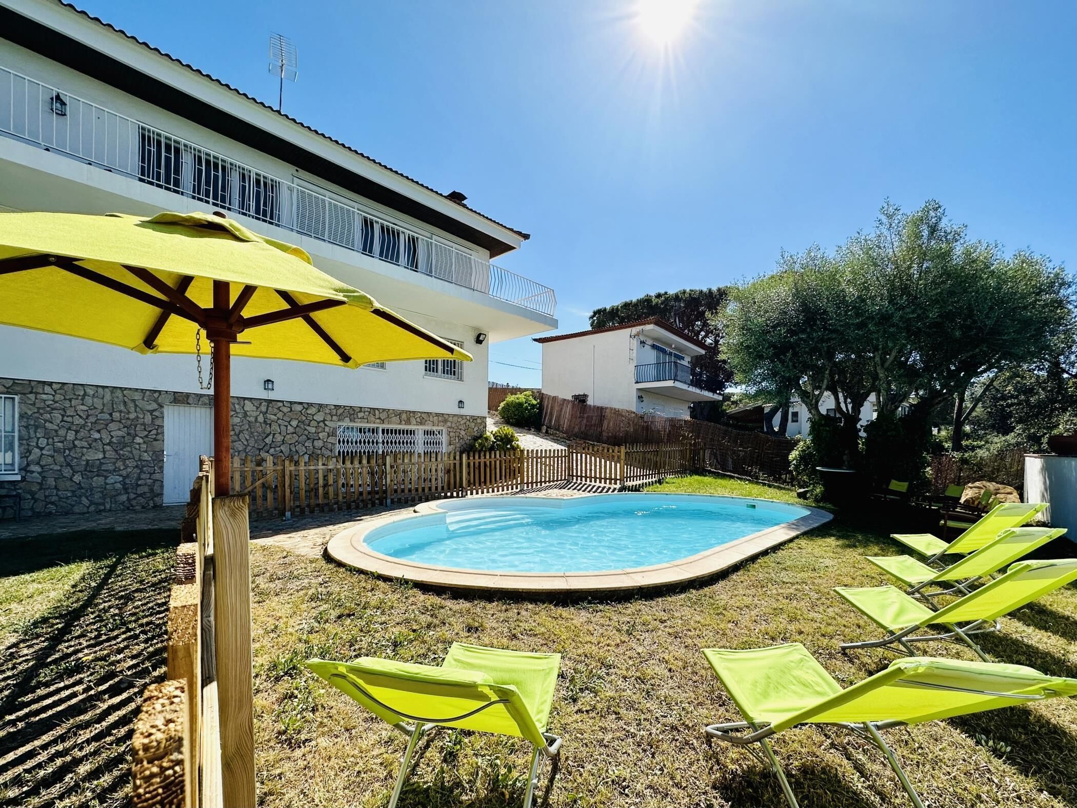 A swimming pool surrounded by a grassy area with lounge chairs and a yellow umbrella.