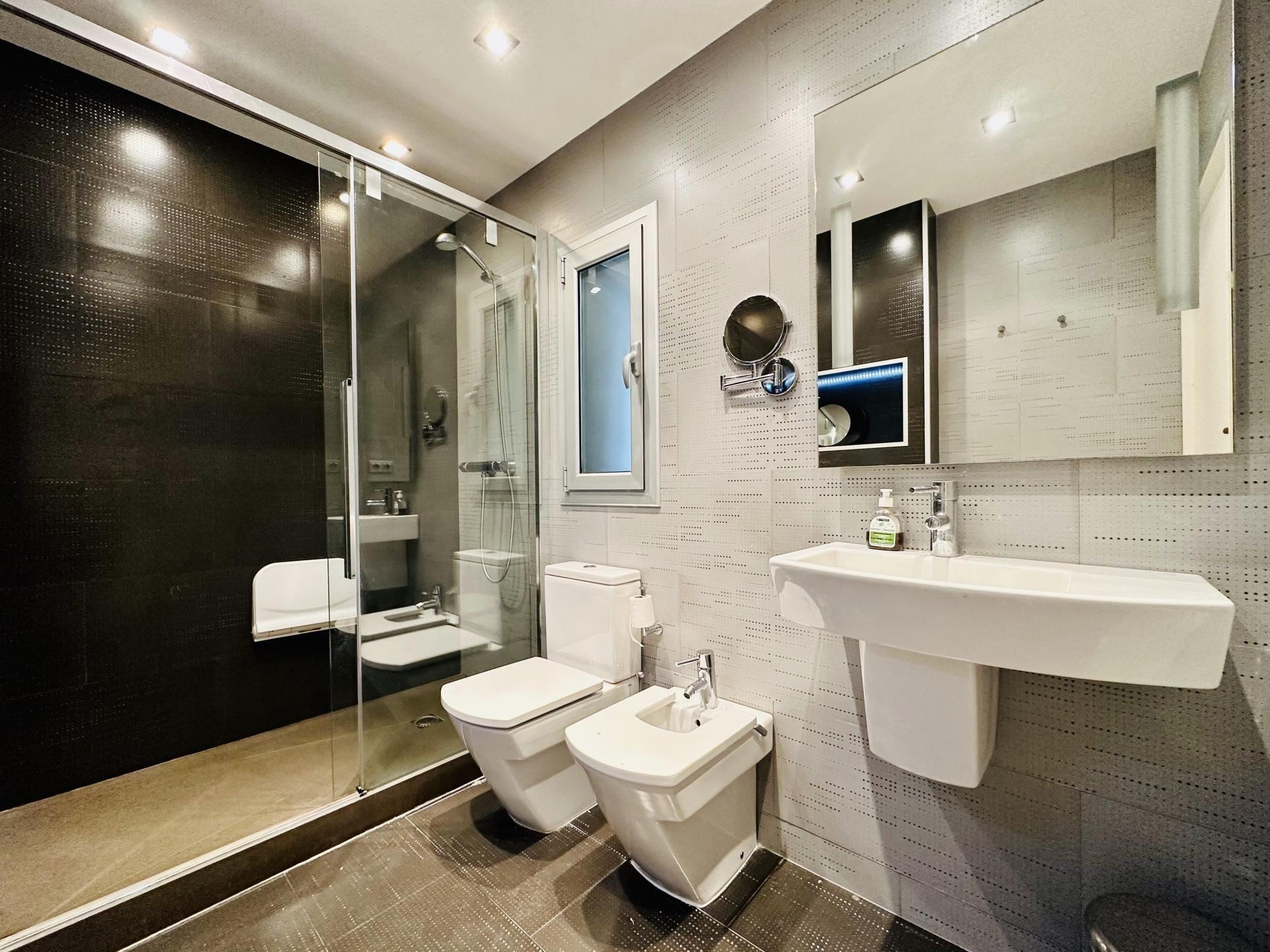 A modern bathroom with a glass-enclosed shower, a white sink, and a toilet.