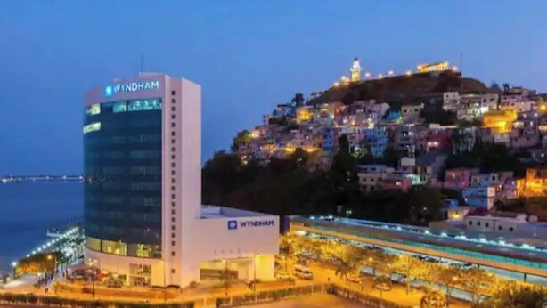 A hotel with a modern design, a prominent 'WYNDHAM' sign, and a view of a hillside with colorful buildings. - Nice apartment, Las Penas-Riverfront 1 (Guayaquil)