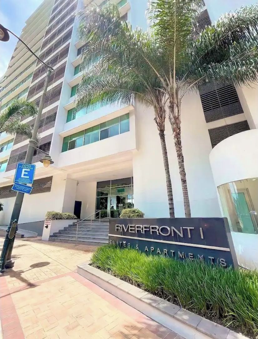 En modern byggnad med en skylt som visar texten ”Riverfront Suites & Apartments”.