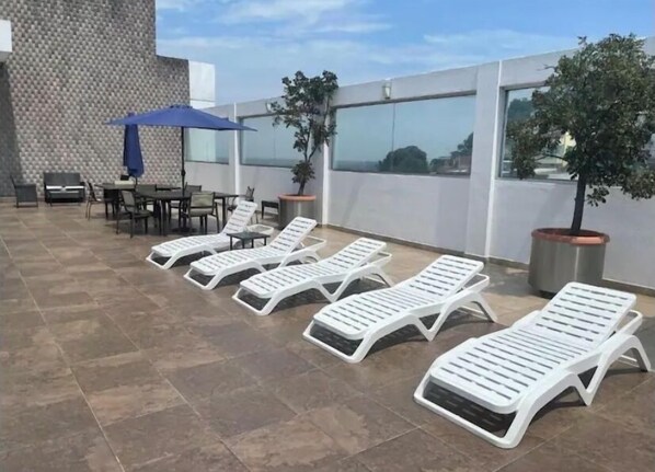 Une terrasse sur le toit, avec des chaises longues, une table et des chaises, ainsi que des plantes en pot.