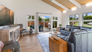 A spacious living room with a wooden ceiling, a large black leather sofa, a wooden coffee table, and a glass cabinet. - AC IN ALL 4 BEDROOMS! Recently renovated 4BD/3B Queen's Bath home w/Jacuzzi! (Princeville)