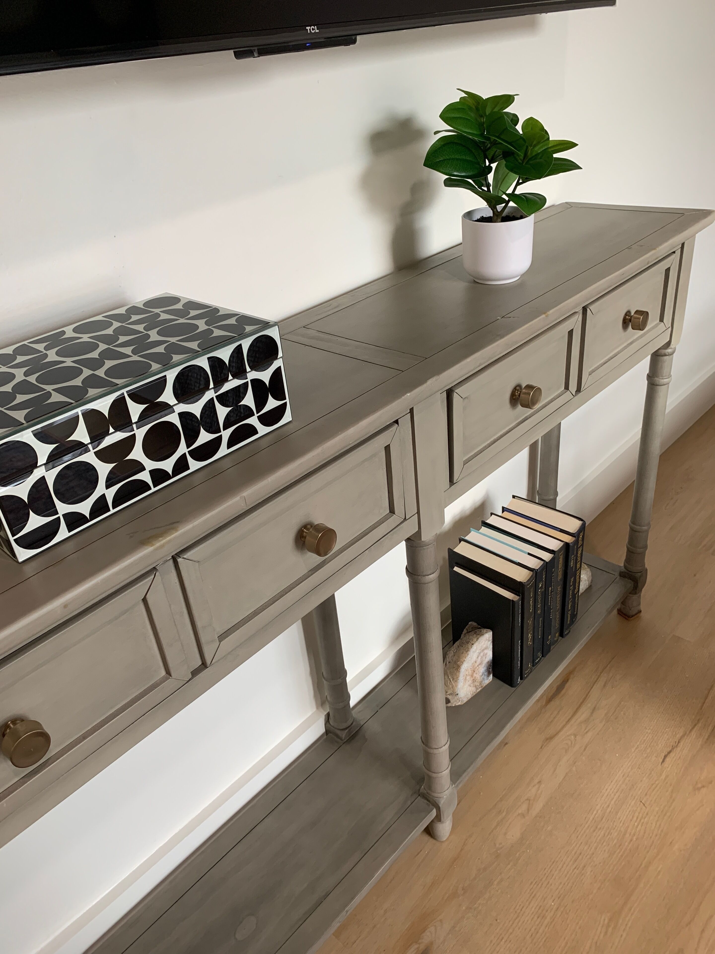 A wooden console table with a geometric-patterned box, a potted plant, and books.