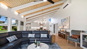 A spacious living room with a large sectional sofa, a round coffee table, and a dining area with a wooden table and chairs. - AC IN ALL 4 BEDROOMS! Recently renovated 4BD/3B Queen's Bath home w/Jacuzzi! (Princeville)