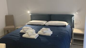 A neatly made bed with a dark blue bedspread and white pillows, a small bedside table, and a wall-mounted light fixture.