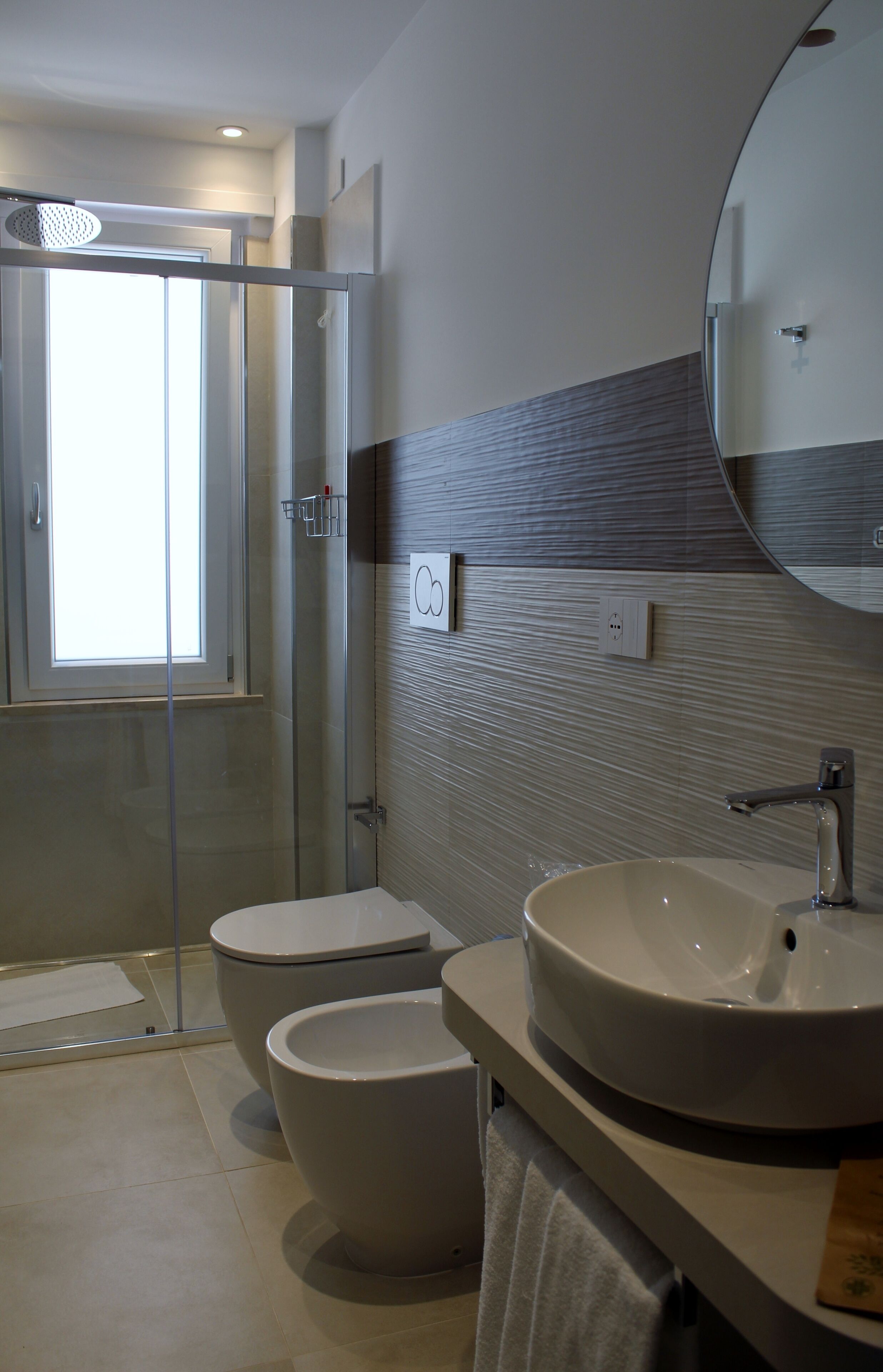 A modern bathroom with a glass shower enclosure, two toilets, a large sink, and a mirror.