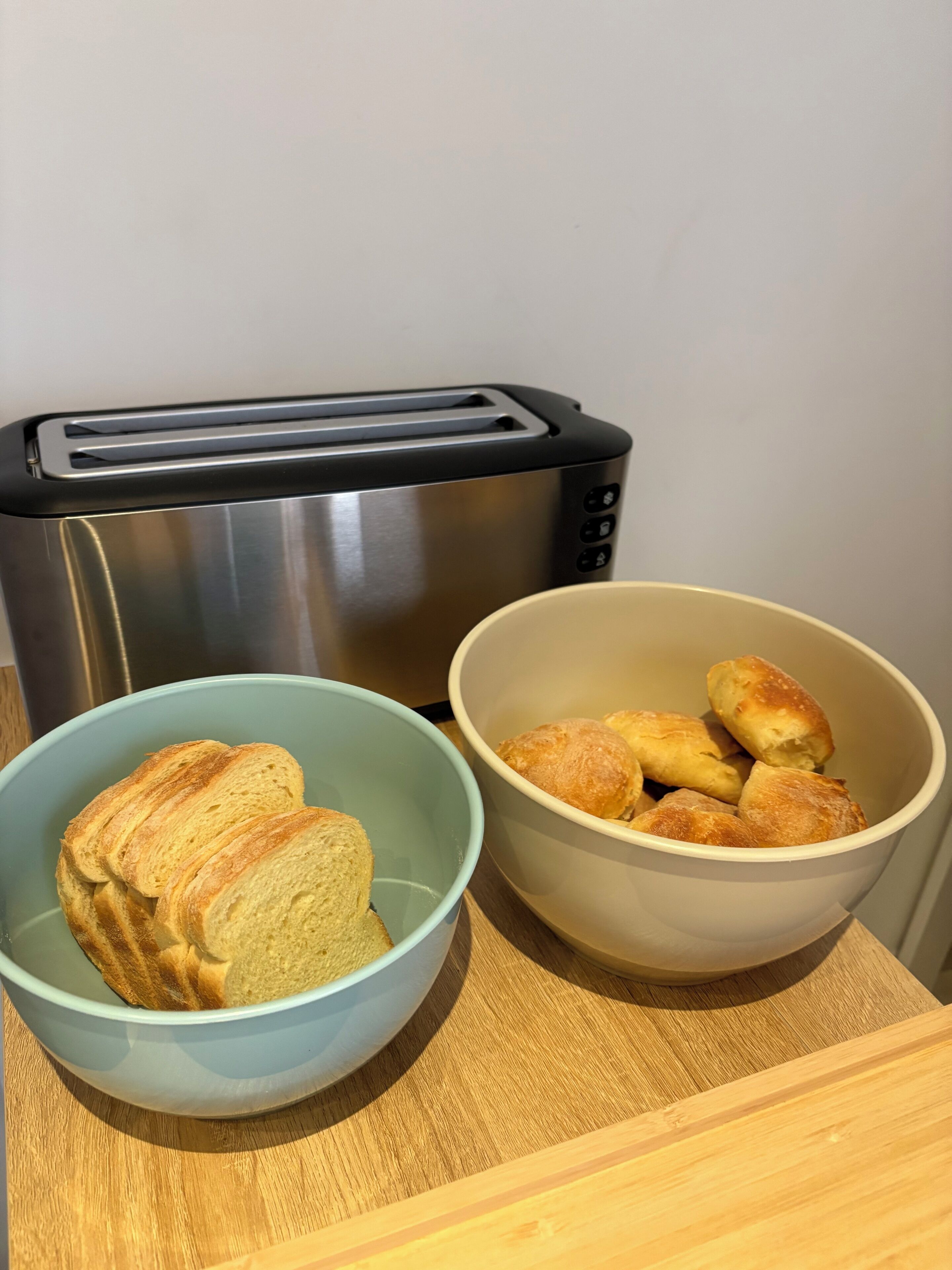 A toaster, two bowls with bread, and a wooden surface.