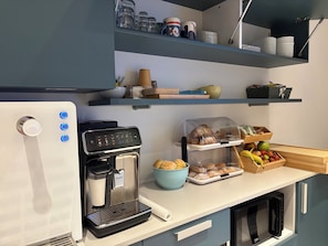 A modern kitchen with a coffee maker, a bread display, and a fruit basket.