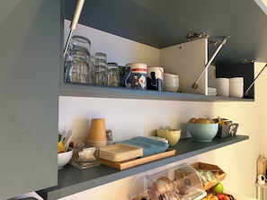 A kitchen with shelves containing glass jars, ceramic mugs, and plates. - Divina Holiday  (Maiori)