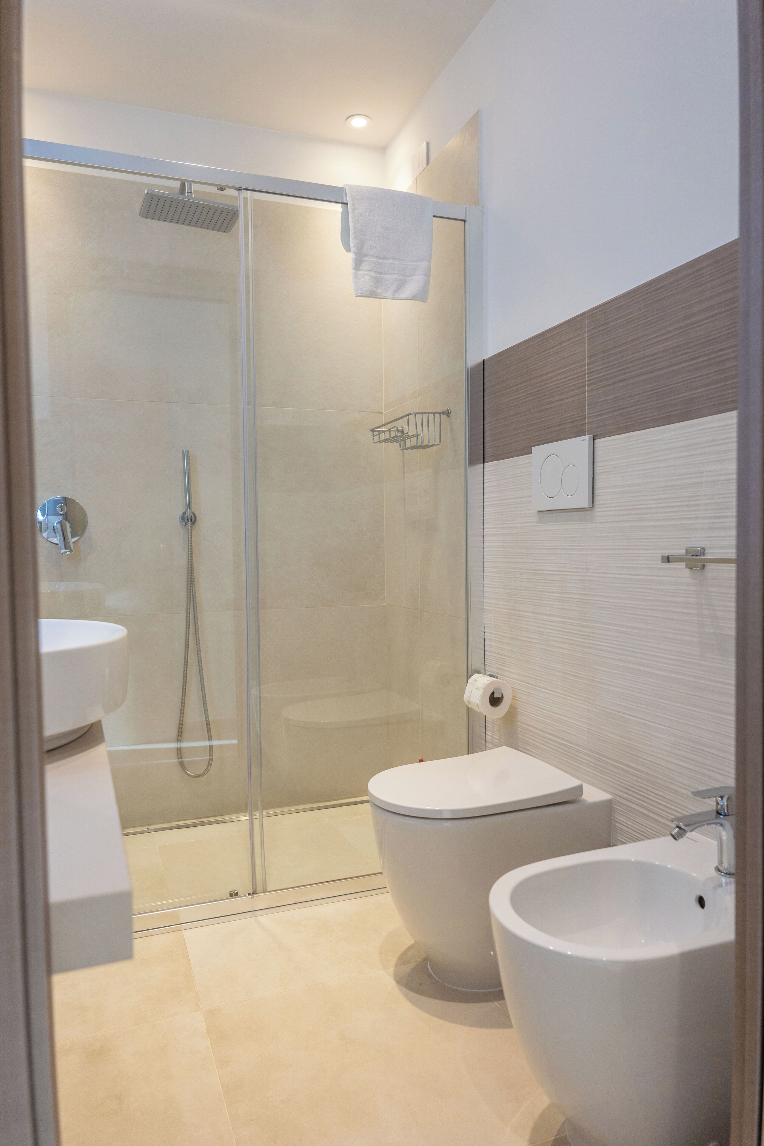 Un bagno moderno con cabina doccia in vetro, un water e due lavabi.