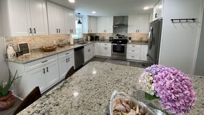 A modern kitchen with white cabinets, granite countertops, stainless steel appliances, and a central island with decorative items. - The Yellowfin Inn- Down East Vacation Home with Sound Side Views (Gloucester)