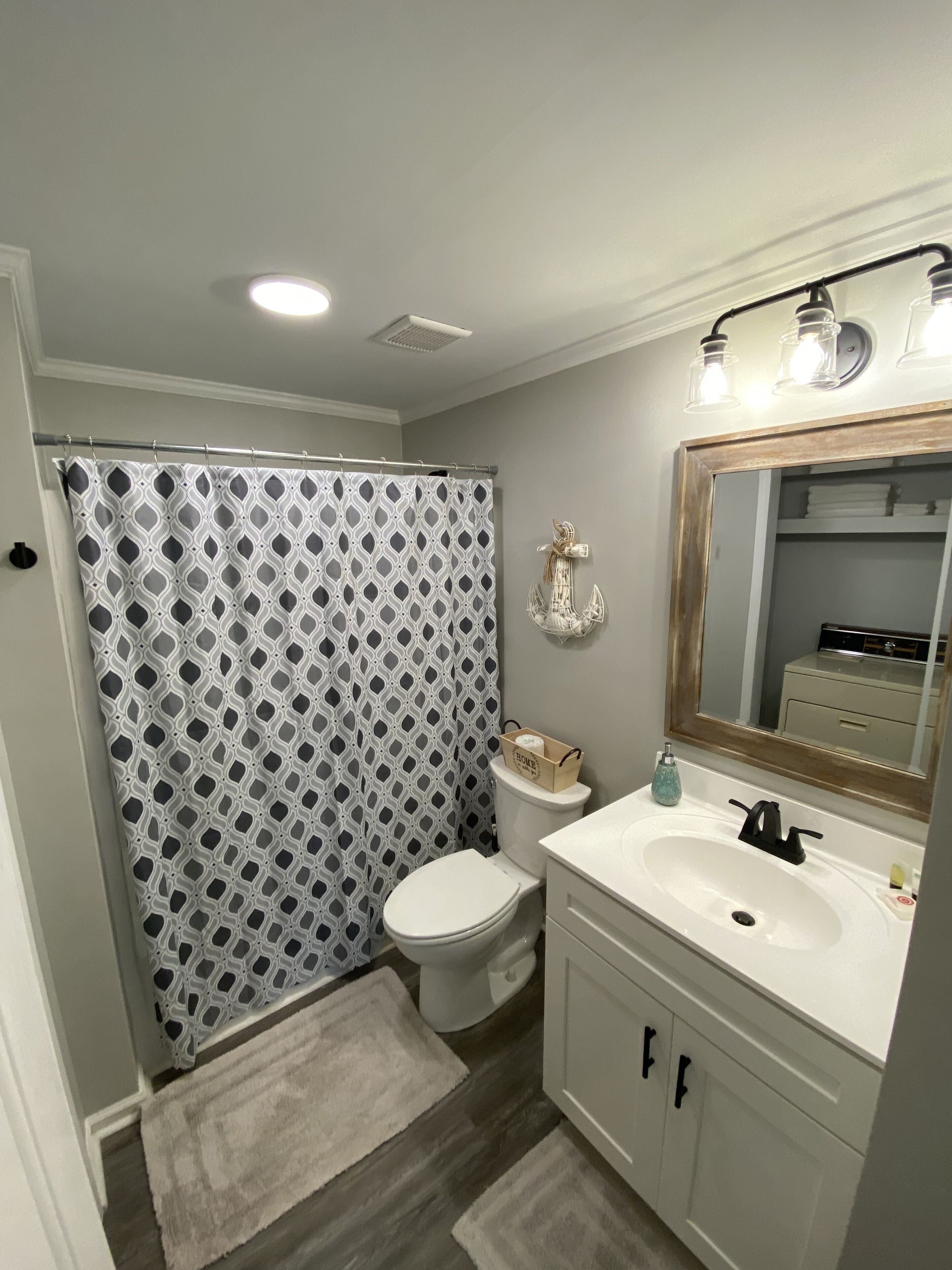 Une salle de bain avec un rideau de douche à motifs, des toilettes, un lavabo avec un miroir et un porte-serviettes.