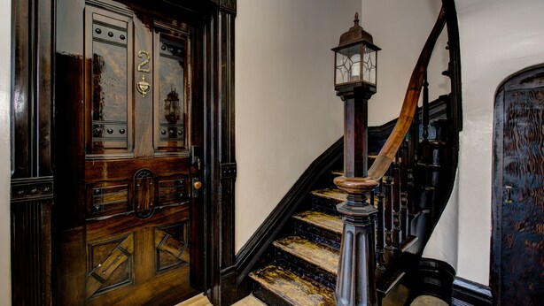 A wooden staircase with a lantern at the top, a door with a number, and a patterned floor.