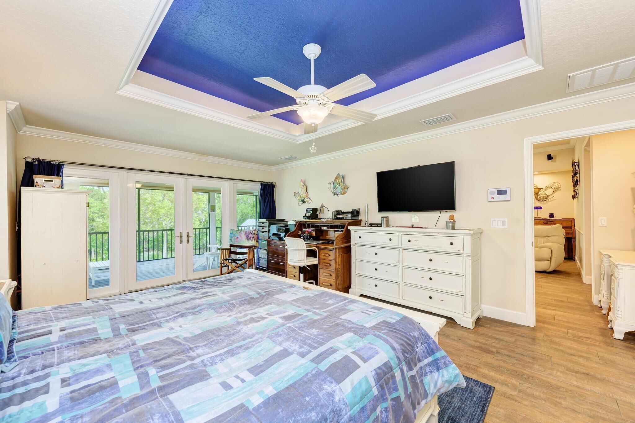 A bedroom with a large bed, a desk, a dresser, a ceiling fan, and a TV.