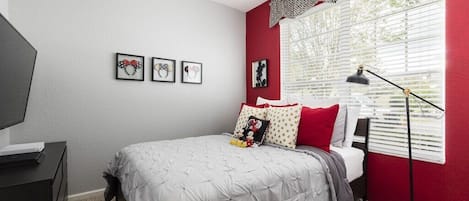 A bedroom with a bed, a desk, a chair, a floor lamp, and a window with blinds.