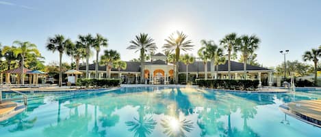 A clear swimming pool with a reflection of palm trees and a building in the background.