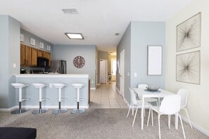 Una cocina moderna con taburetes de bar, una mesa de comedor con sillas y un reloj en la pared.