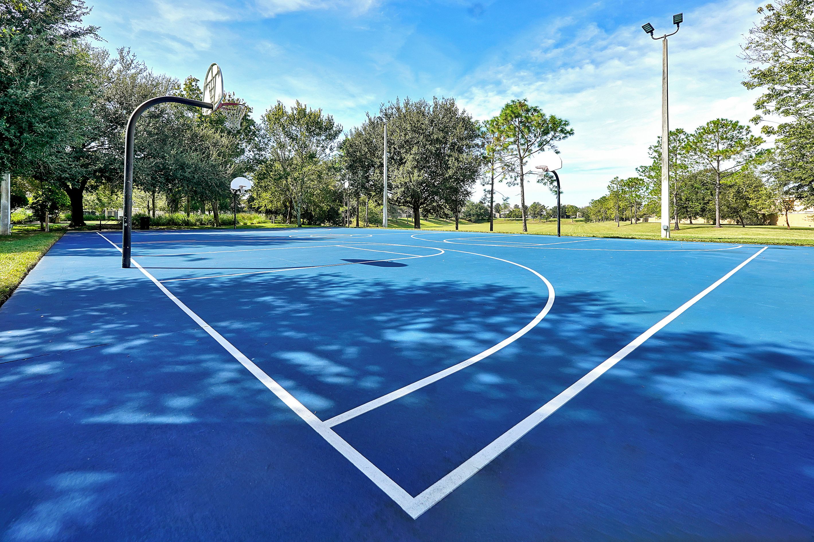 Una cancha de baloncesto al aire libre con superficie azul, líneas de demarcación blancas y aro.