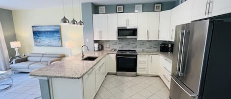 Una cocina moderna con armarios blancos, un refrigerador de acero inoxidable, un microondas y una estufa. Hay un comedor con una mesa y sillas.