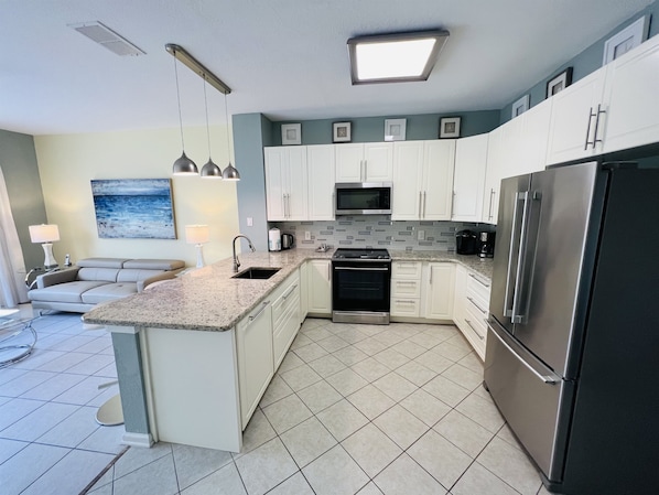 Una cocina moderna con armarios blancos, un refrigerador de acero inoxidable, un microondas y una estufa. Hay un comedor con una mesa y sillas.