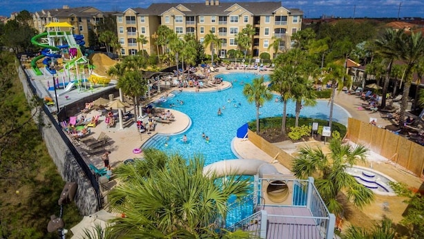 Um resort com uma piscina grande, palmeiras e um tobogã.