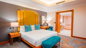 Una habitación de hotel con una cama grande, dos mesitas de noche, un banco, un escritorio y un espejo.