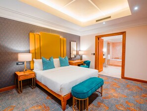 Une chambre d’hôtel avec un grand lit, deux tables de chevet, un banc, un bureau et un miroir.