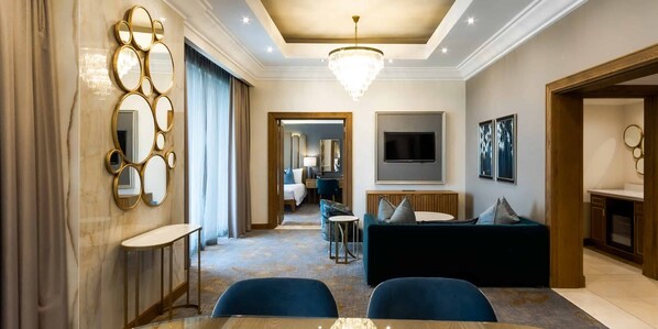 Une chambre d’hôtel moderne comprenant un coin repas, un salon avec un canapé et une télévision, ainsi qu’un couloir menant à la salle de bain.
