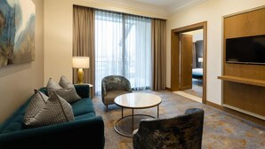 Habitación de hotel con sofá, sillón, mesa de centro redonda y televisión montada en la pared.