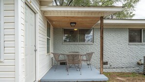 Un patio cubierto con una mesa y sillas, techo de madera y pared de piedra.