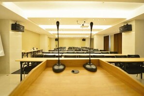 A conference room with rows of tables and chairs, a podium, and a ceiling-mounted projector. - Elegant Stay Hotel (Shantou Jinhul Road Store) (Shantou)