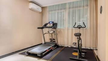 A room with a treadmill, a stationary bike, and a yoga mat.