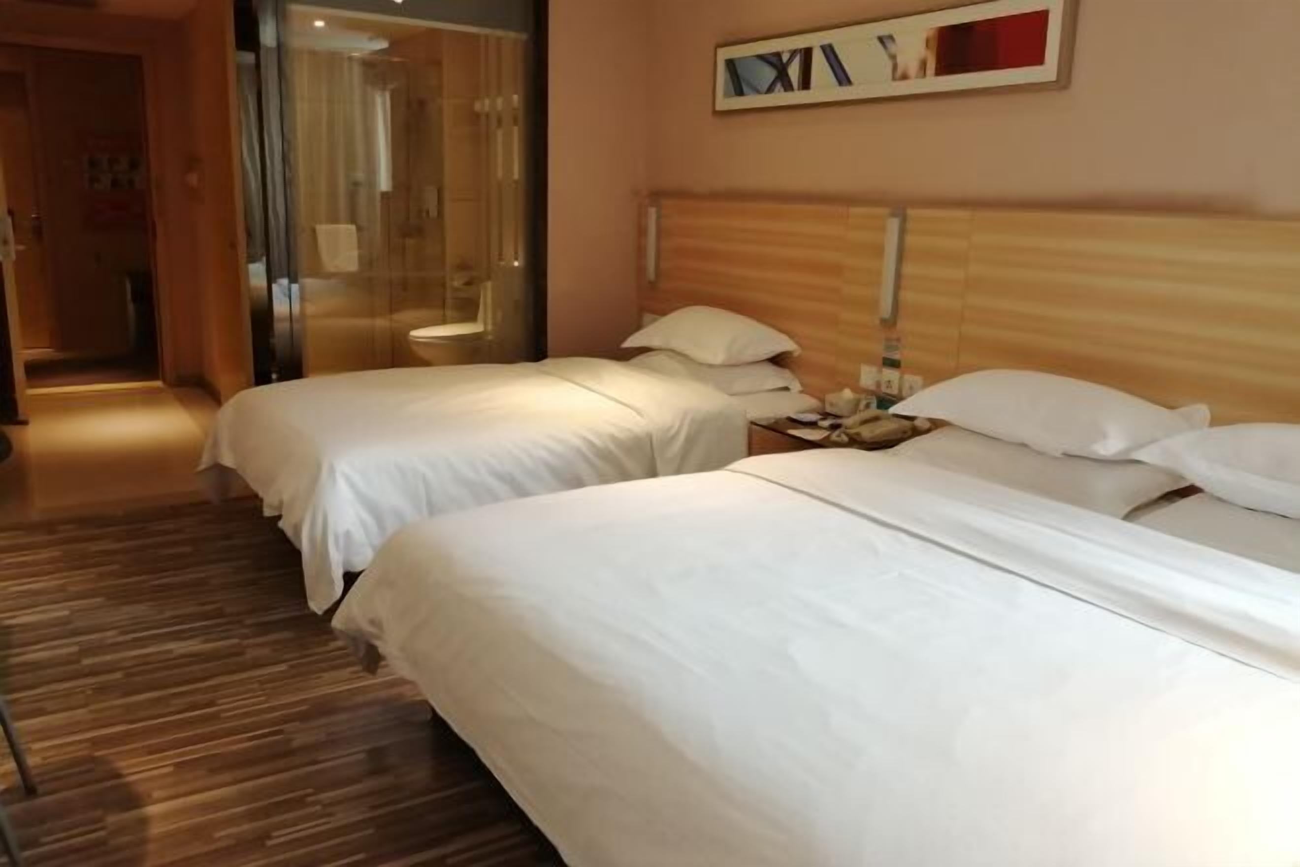 A hotel room with two beds, a wooden headboard, a bedside table with a lamp, and a mirror on the wall.
