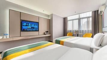 A hotel room with two beds, a television mounted on the wall, a window with curtains, and a small table with chairs.