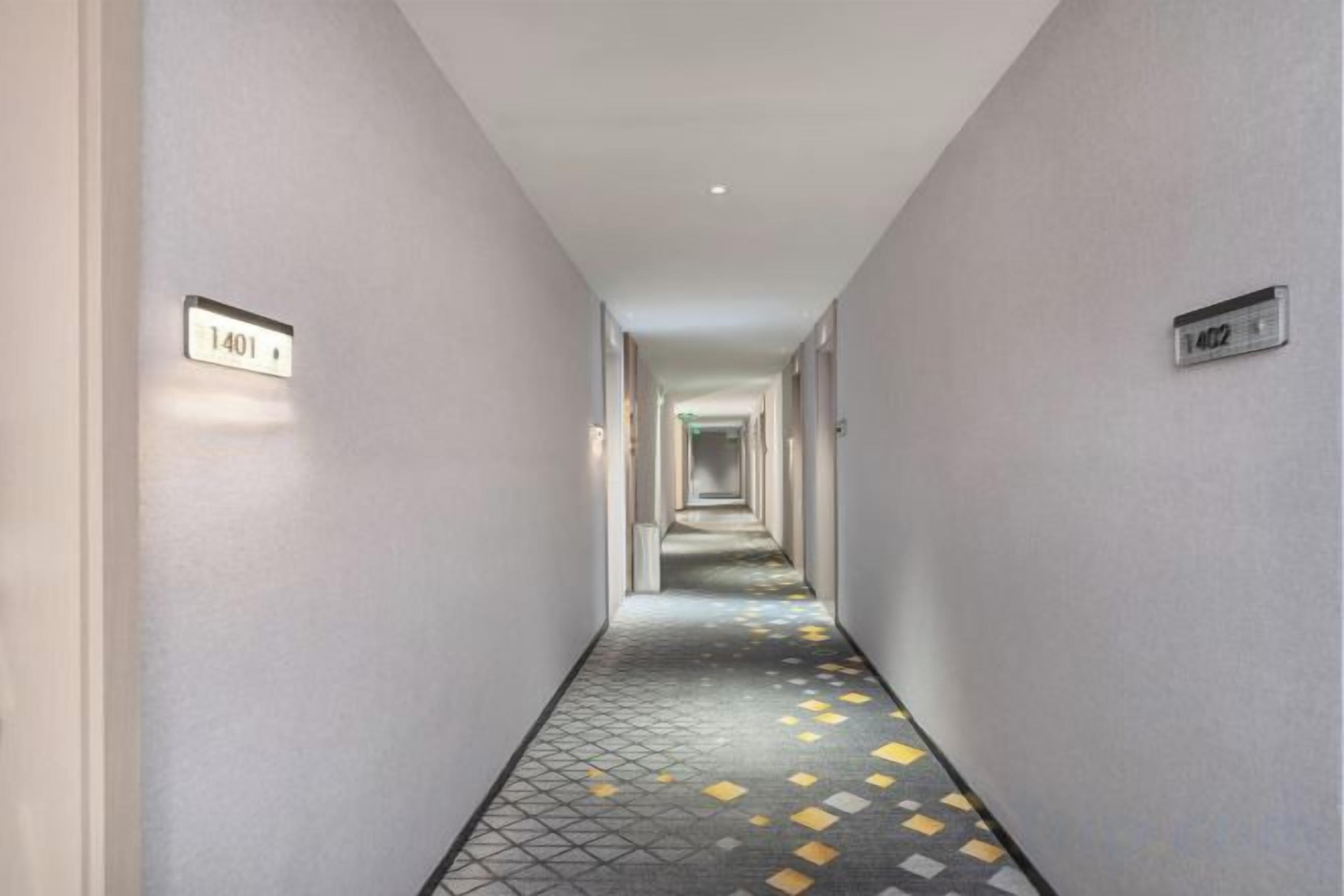 A corridor with a patterned floor and numbered doors, leading to a hallway.