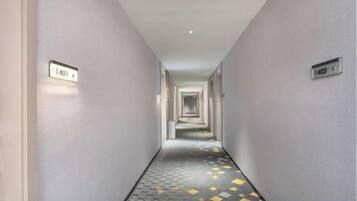A corridor with a patterned floor and numbered doors, leading to a hallway.