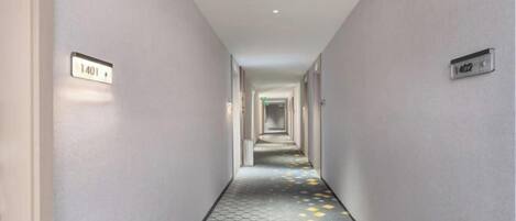 A corridor with a patterned floor and numbered doors, leading to a hallway.