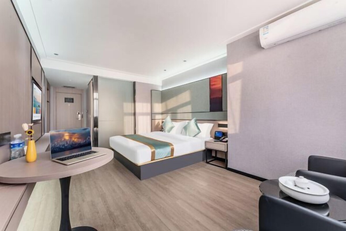 Ein modernes Hotelzimmer mit einem Bett, einem Schreibtisch mit Laptop, einem kleinen Tisch mit Teller und einem Stuhl.