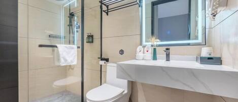 Un baño moderno con cabina de ducha de vidrio, inodoro blanco, lavamanos de mármol y un espejo.