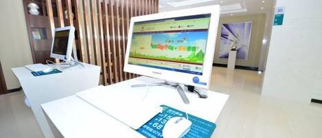 A reception desk with a computer monitor displaying a colorful interface, a mouse on a mat, and a wooden partition in the background.
